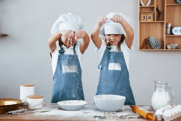 istock Two little girls in blue chef uniform working with flour on the kitchen 1323874725