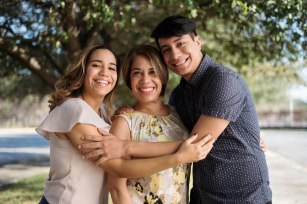 Latin mother with two children standing outside and smiling A latin mother with the children standing outside, embracing and smiling at the camera. mom and sister stock pictures, royalty-free photos & images