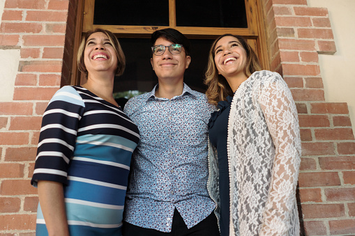 Cheerful latin mother and her young adult children embracing, looking up and smiling.