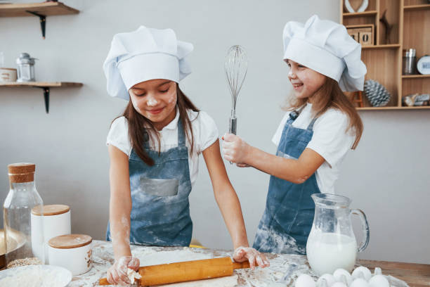 istock Two little girls in blue chef uniform kneading dough on the kitchen 1323876510