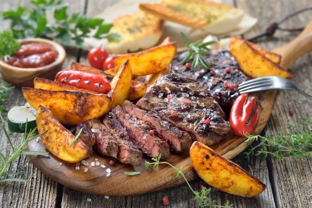 Grilled beef steak with rosemary potato wedges, dipping sauce and herb baguette