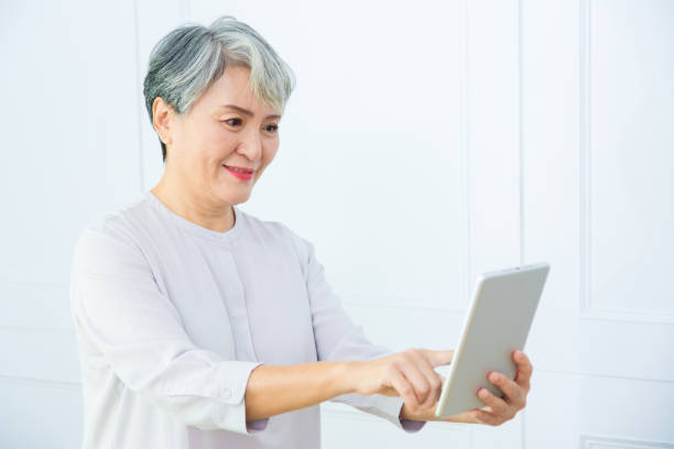istock Smiling middle-aged Asia woman browsing wireless Internet on tablet at home, happy modern senior female using pad device, elderly technology concept. 1323883241