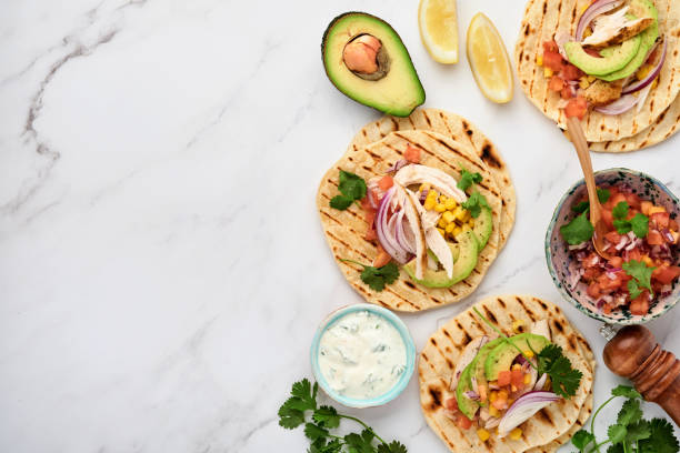 Mexican tacos with grilled chicken, avocado, corn kernels, tomato, onion, cilantro and salsa at white stone table. Traditional Mexican and Latin american street food. Top view.