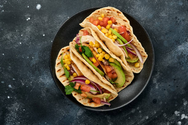 istock Mexican tacos with grilled chicken, avocado, corn kernels, tomato, onion, cilantro and salsa at black stone table. Traditional Mexican and Latin american street food. Top view. 1323885053