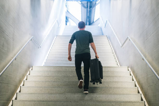 istock Young man carries suitcase up staircase in train station 1323886309