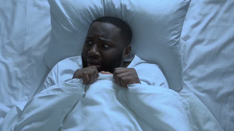 Adult Black man scared of noise hiding under blanket, infantility