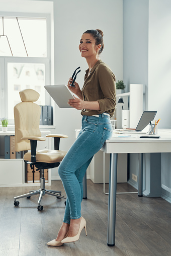 Full length of young woman in smart casual wear smiling while standing in the office