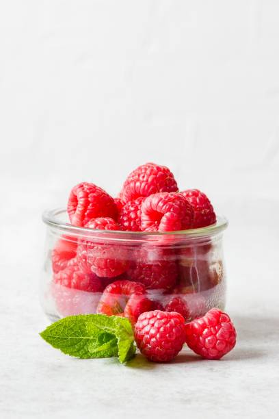 istock A small jar filled with fresh and ripe raspberries and a small sprig of mint before a rustic white background 1323892783