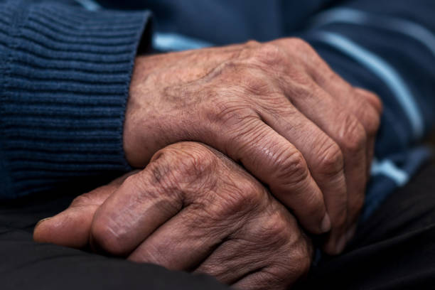 istock Old man holds interlocked wrinkled hands on lap. 1323895528