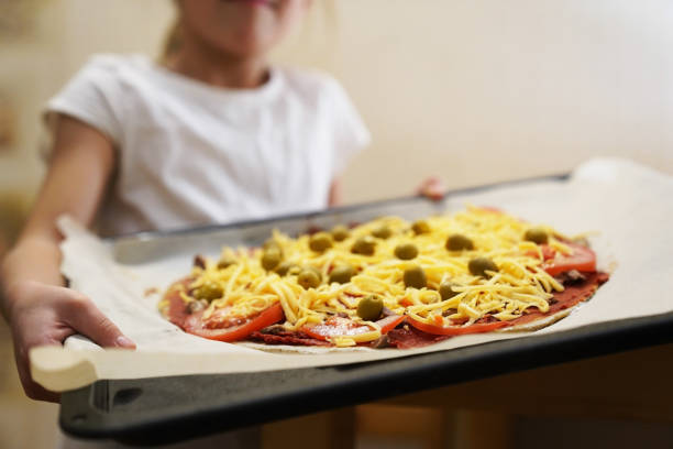 a garota segura uma assadeira preparada para assar pizza com carne. cozimento. - bread food baked 7 grain bread - fotografias e filmes do acervo