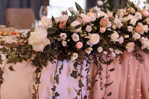 Wedding. Banquet. The festive table for guests, decorated with a composition of white and pink flowers and greenery, there are candles, served with crockery in restorane.