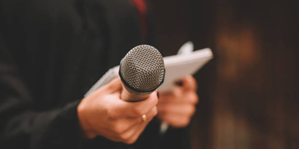 istock Journalist at news conference, writing notes, holding microphones 1323899386