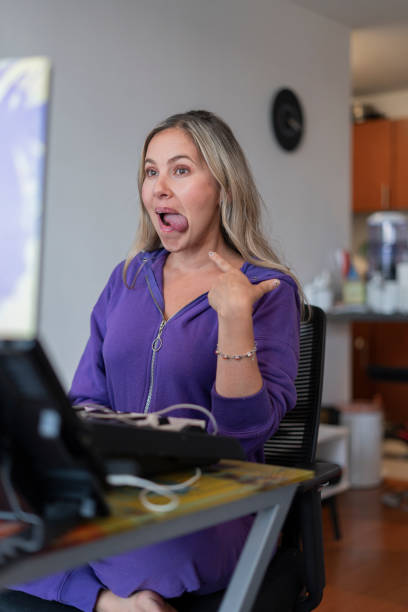 The singing teacher performs mouth and tongue exercises while giving her virtual singing classes wearing her pajamas from home.