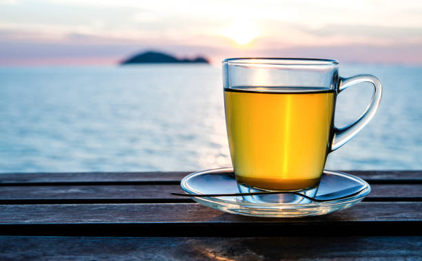 tasse de thé vert devant la lumière du coucher du soleil sur table en bois. - at the beach photos et images de collection