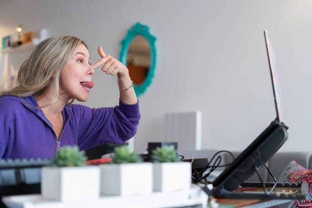 The singing teacher performs mouth and tongue exercises while giving her virtual singing classes wearing her pajamas from home.