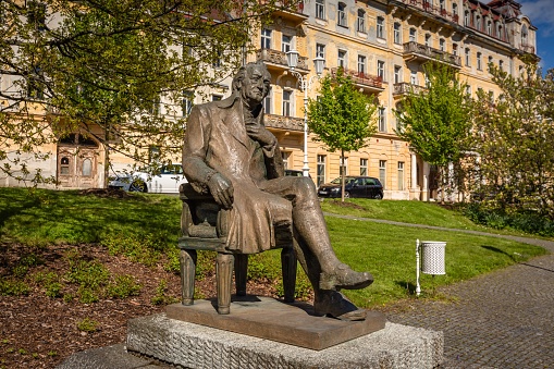 Marianske Lazne, Czech Republic - May 30 2021: Statue placed on  Goethe square in a spa city. Green lawn and trees behind. Sunny spring day.