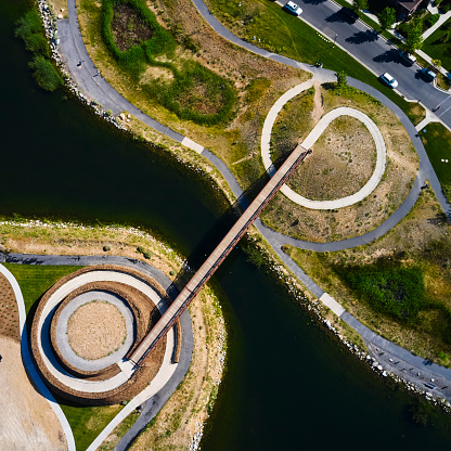 A top down aerial view of a pedestrian bridge over a small lake.