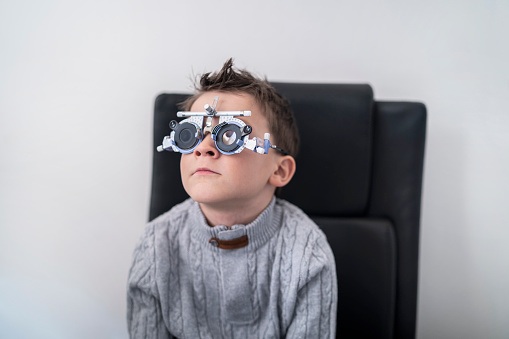 Young boy sits patiently, wearing the special glasses to proceed with his eye test to see if he needs glasses.