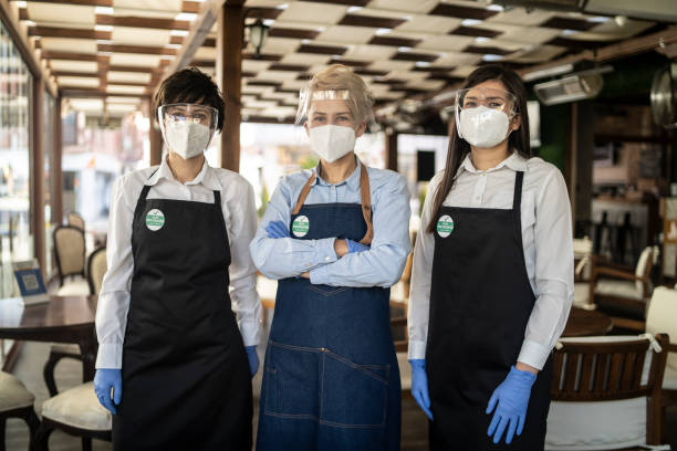 istock Restaurant owner and waitresses working at a restaurant, wearing a double protective face masks and a badge showing that they are vaccinated against COVID-19. 1323919019