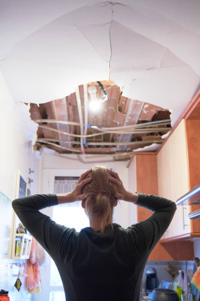 Woman with her hands on her head comes home to find that the kitchen ceiling has collapsed. Concept of accident at home