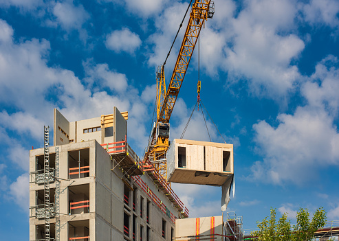 Crane lifting a prefabricated wooden building module to its position in the structure.