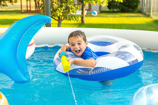 Young boy in a blue and white swim ring using a water blaster in the swimming pool.
