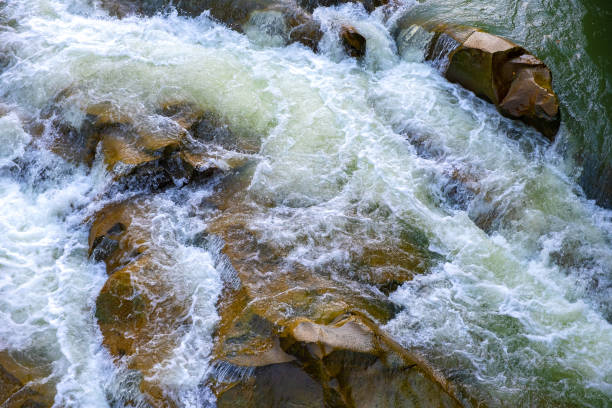 istock Mountain river with small waterfall with clear turquoise water falling down between wet boulders with thick white foam. 1323926506