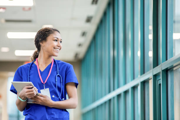 joven enfermera mirando por la ventana del hospital sonriendo - medical student fotografías e imágenes de stock
