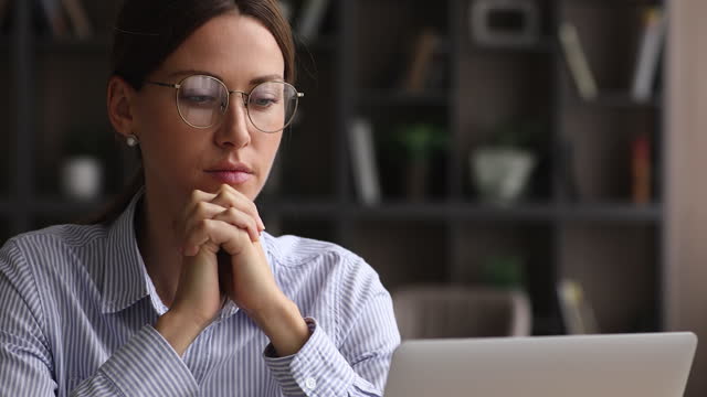 Thoughtful woman lost in thoughts sit in front of laptop