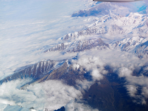 Brown snowy mountains under the clouds. View from the airplane window. Travel concept