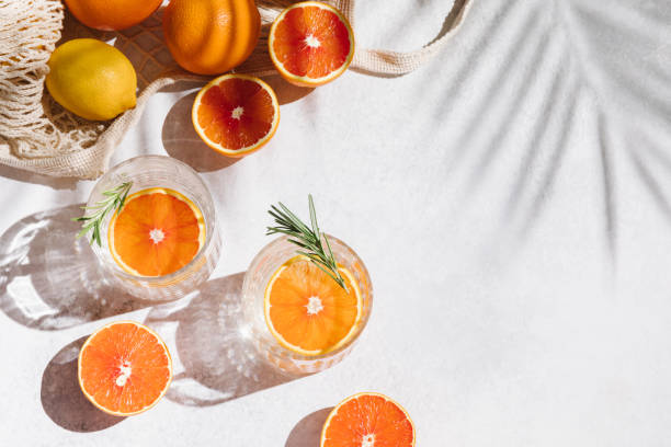 Summer orange cocktails with fresh citrus fruits. Hard seltzer, lemonade, refreshing drinks, low alcohol mocktails, summer party concept. Trendy shadow and sunlight. Flat lay, top view, copy space. stock photo