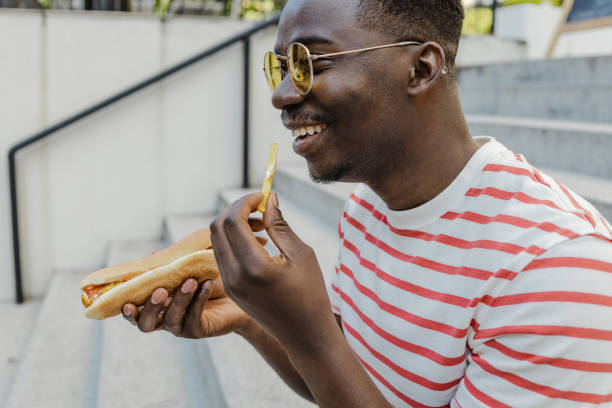 istock Young African-American man is eating hot dog and smiling 1323930708