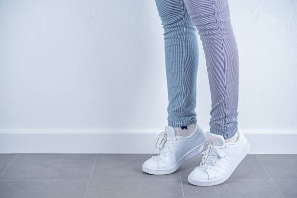 istock Women's feet in white sneakers on a white background 1323935138