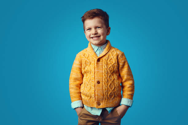 istock Kid smiling while holding hands in pockets, isolated over blue background 1323935250