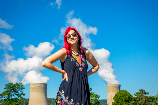 A beautiful 19 year old female standing in front of a nuclear power plant.