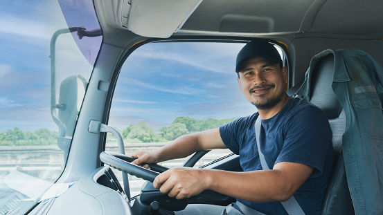 Professional truck driver bearded man smiling confident fasten seat belt While driving. concept business owner Transportation delivery semi-truck