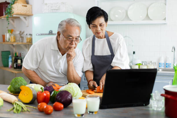 Portrait of an elderly Asian couple. Tutorial Online cooking is in the kitchen at home. Senior couple watching video recipes on the laptop at the kitchen. The concept of leisure hobby of retirement stock photo
