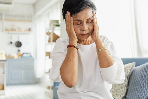 An elderly Asian woman uses her hand to grasp the head. Old women have dizziness and headache due to stress. She has a congenital disease. The health concept of retirement