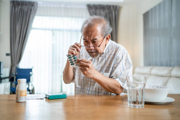 asian senior elderly male patient on eating table at nursing home care. older man wearing eyeglasses and look to medicine pill in blister pack, read prescription and content. medical insurance concept - blister pack pill medicine healthcare and medicine imagens e fotografias de stock