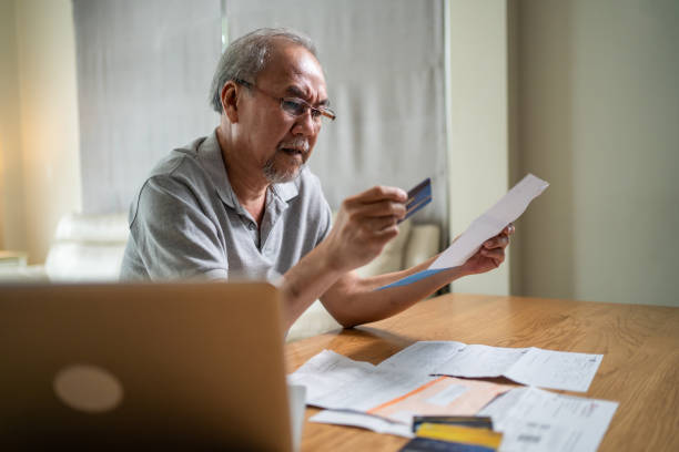 Depressed desperate Asian Senior Elderly male feeling worried about financial problem. Stressed older man looking frustrated to paperwork and bills think of money debt, budget loss, bankruptcy at home