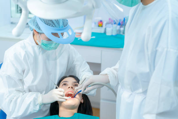 Asian expert dentist doctor wear PPE and mask examine patient's teeth at dental clinic. Dental assistant use suction to keep young girl's mouth dry due treatment procedures during Coronavirus pandemic el médico dentista experto asiático usa epp y máscara examina los dientes del paciente en la clínica dental. asistente dental utiliza succión para mantener la boca seca de la niña debido a los procedimientos de tratamiento durante la pandemia de coro