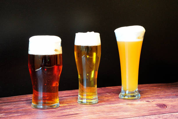 trzy szklanki różnych rodzajów piwa z białą pianką stoją w rzędzie na drewnianym stole. - draught beer variation three objects zdjęcia i obrazy z banku zdjęć