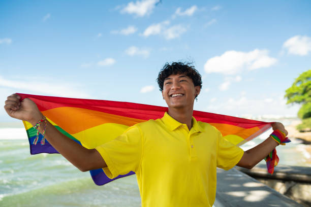 jovem gay orgulhosamente segurando a bandeira lgbt em suas mãos - flag gay man american culture rainbow - fotografias e filmes do acervo