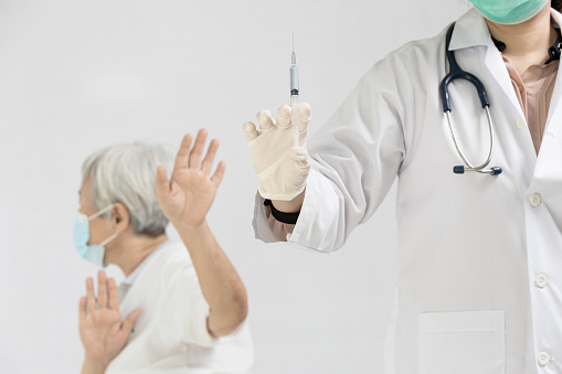 Hands of doctor preparing a syringe to inject the elderly,old people showing distrustful of COVID-19 vaccine,rejecting medicine,refusing to receive a Coronavirus vaccine injection,vaccination concept