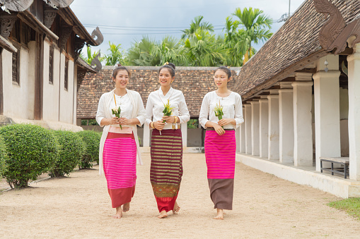 Portrait of group of Asian Shan women girls, Tai Yai, northern Thai people with traditional Lanna clothes holding flowers at Wat Ton Kwen temple, lanterns decoration. Culture lifestyle.