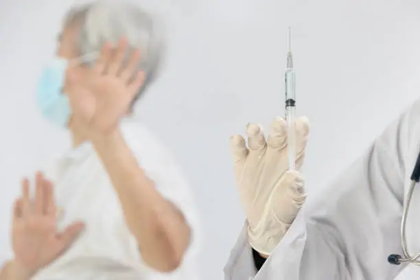 Photo of Hands of doctor preparing a syringe to inject for elderly,stop hand gesture,senior woman rejecting preventive medicine during Coronavirus pandemic,stop vaccination,refusing to receive COVID-19 vaccine