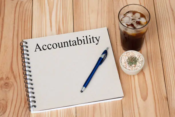 Photo of Accountability concept on notebook, pen cactus and coffee cup on wooden table. Business concept.