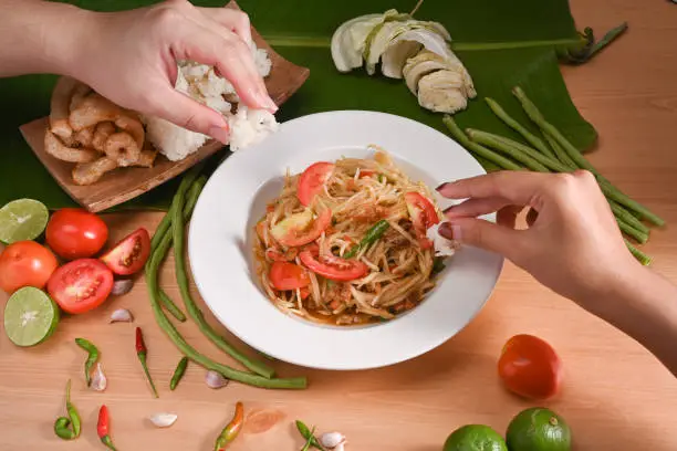 Photo of Two woman eating sticky rice with green papaya salad by their hand.