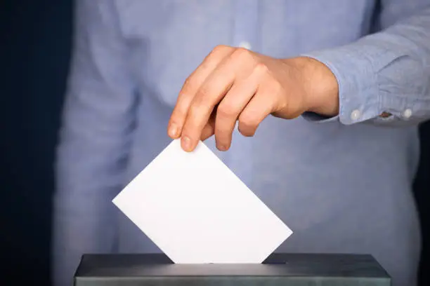 Hand of a voter putting vote in the ballot box. Election concept.