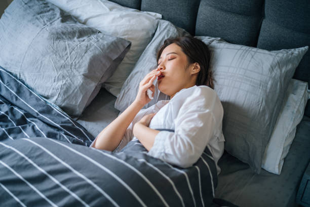 Sick woman blowing her nose, she covered with blanket Shot of an attractive young Asian woman suffering with the flu while lying in on her bed at home bed of hay stock pictures, royalty-free photos & images